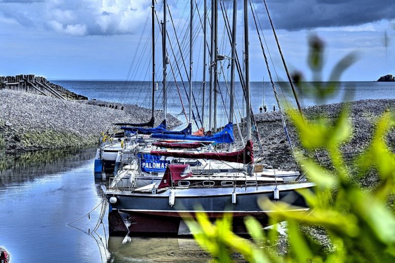 Sailing boats moored in a narrow harbour beside a shingle beach