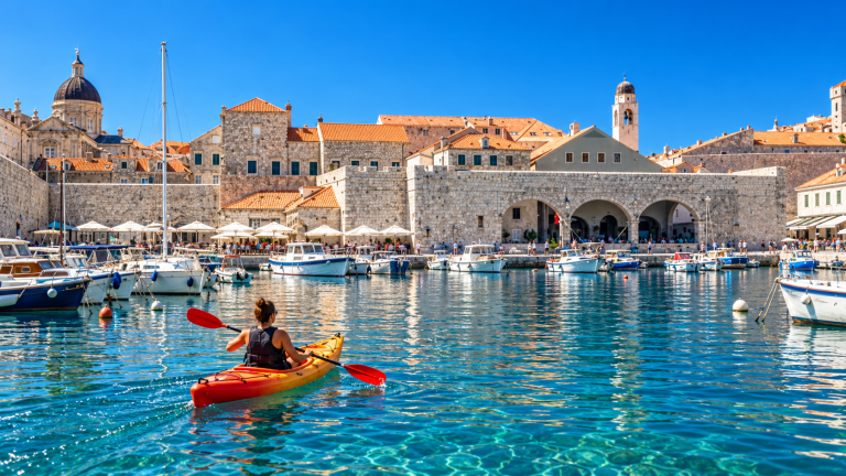 Woman kayaking in Dubrovnik harbour towards the stone walls and waterfront buildings