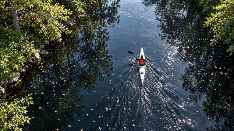 Solo paddler kayaking the River Wye in a white kayak between tree-lined banks.