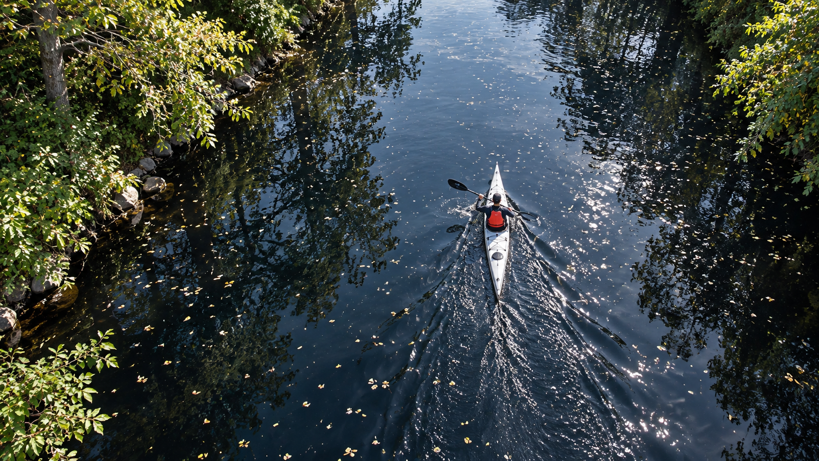 Solo paddler kayaking the River Wye in a white kayak between tree-lined banks.