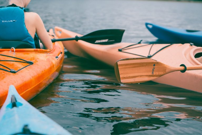Kayaker holding a paddle beside orange and blue kayaks on the water