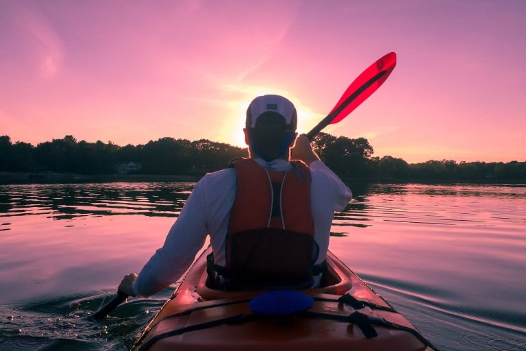 Paddler in a kayak beneath a pink sunset
