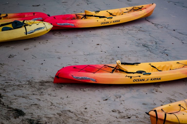 Red and yellow sit-on-top kayaks resting on sand