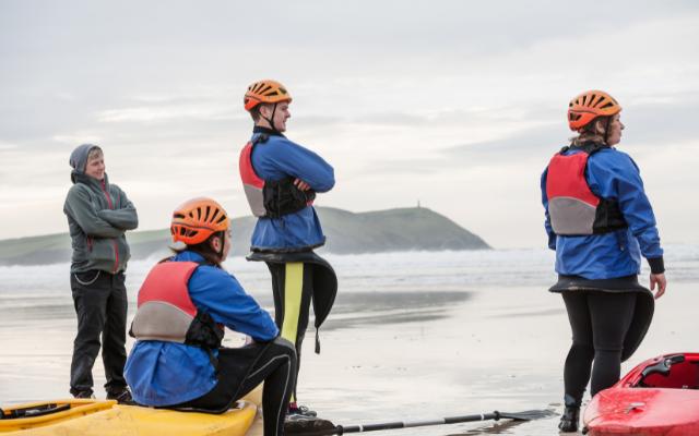 Kayakers wearing helmets and buoyancy aids beside a beach