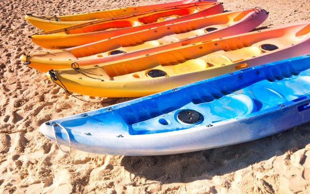 Colourful sit-on-top kayaks lined up on a sandy beach