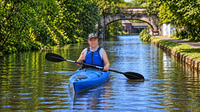 Mark kayaking in Leeds in a blue kayak on the canal, with a stone bridge behind him