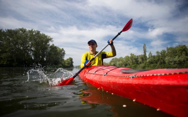 Paddler in a red kayak on a tree-lined river