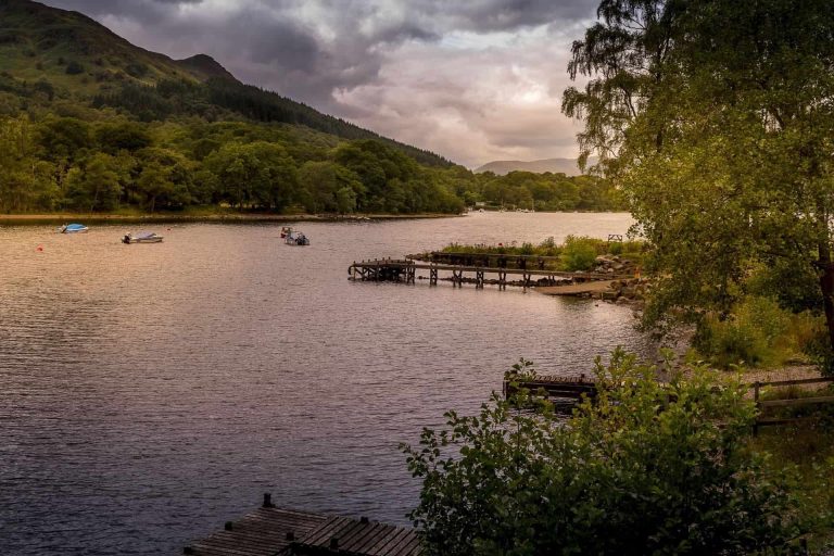 A small jetty on Loch Lomond with wooded hills and mountains beyond