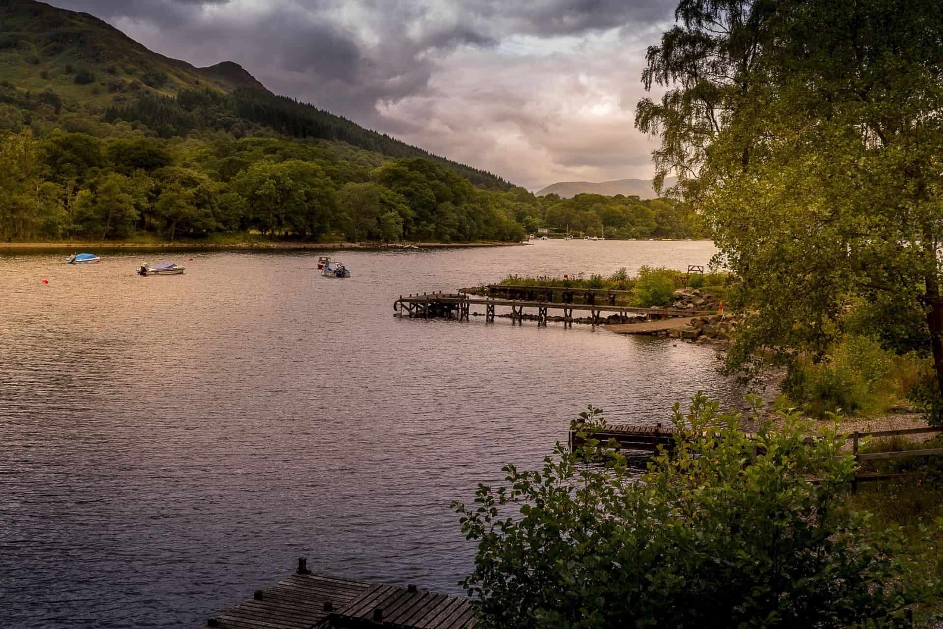 A small jetty on Loch Lomond with wooded hills and mountains beyond