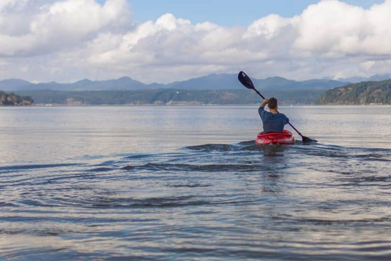 A kayaker paddling a red kayak towards distant hills on Loch Lomond