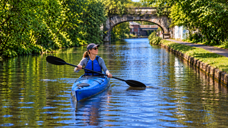 Illustration for kayaking in Leeds: a paddler in a blue kayak on a leafy canal beside a stone bridge